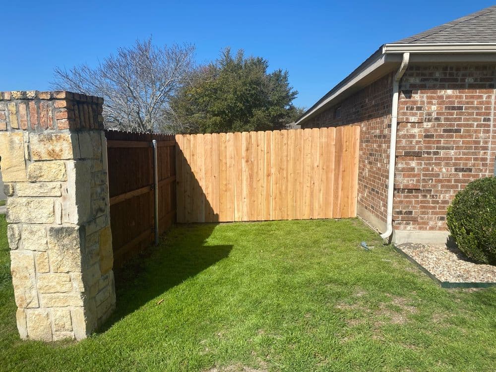 Wooden fence in a backyard with green grass and brick wall accents on a sunny day.