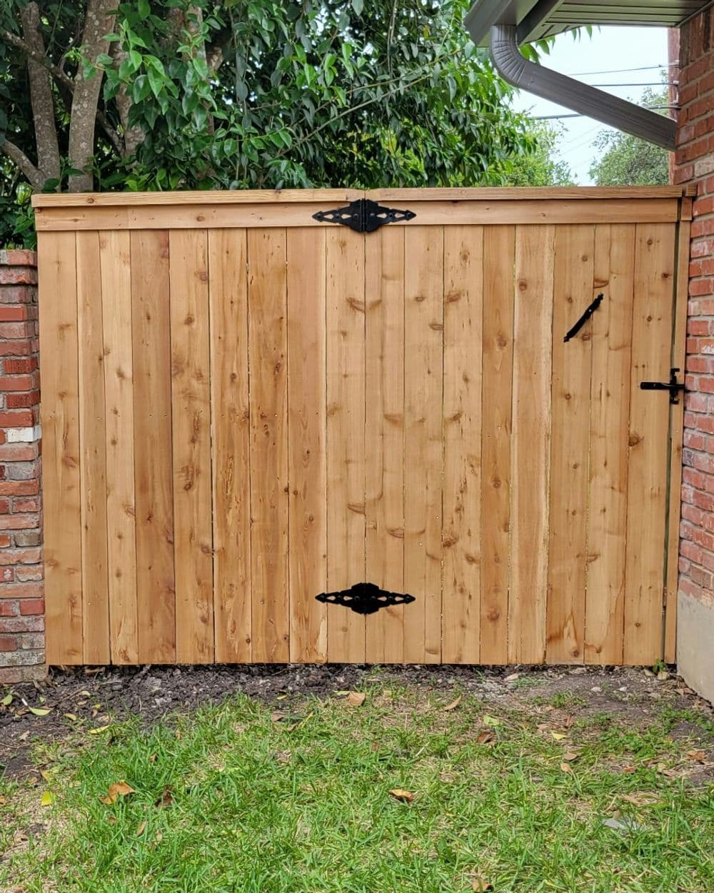 Wooden garden gate with black hardware, set in a brick wall and surrounded by greenery.