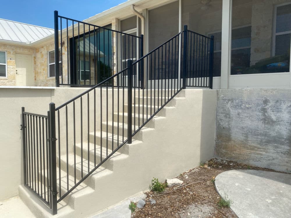 Black railing on outdoor staircase leading to house with stone walls and windows.
